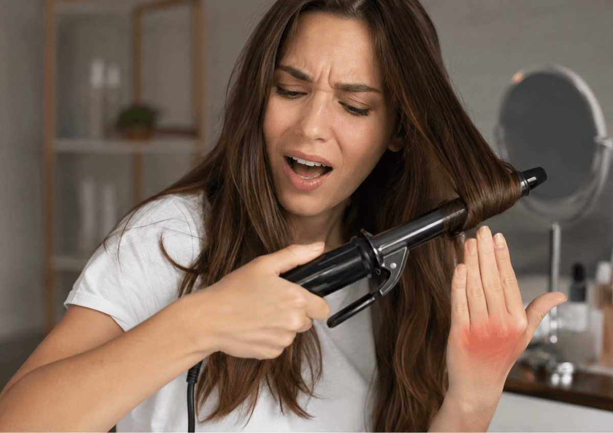 Woman accidentally burning her fingers while using a hair straightener with styling tips for safer heat styling
